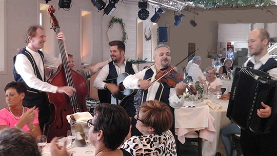 Muzikanten spelen ambiance muziek tussen de tafels in een feestzaal, het publiek klapt enthousiast mee